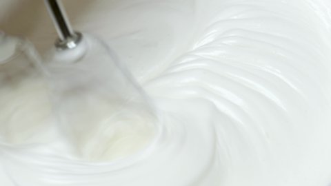 Electric mixer whips egg whites into fluffy cream. Texture thick marshmallow cream is formed while beating, close up shot of custard's texture