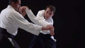 Two Masters participants of the training in special clothes of aikido hakama work out the methods of single combat on spotlights background. Slow motion. Close up. - Powered by Shutterstock - Get 15% off with code: PIKWIZARD15