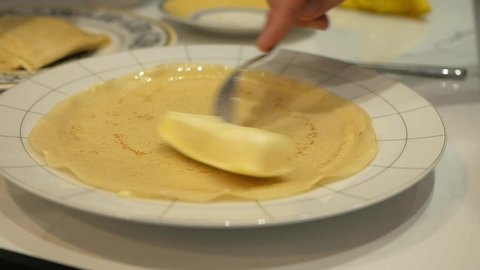 A female hand using a green silicone spatula puts butter on a traditional Russian pancake, which is roasted and baked on a griddle. Butter melts on Russian pancake. Cooking Russian pancakes, close-up.