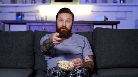 Man watching tv and eating popcorn at home.