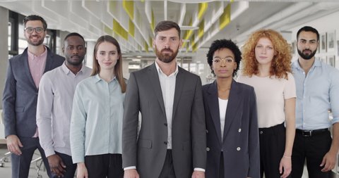 Positive multiracial company staff standing and crossing hands in office. Group of successful mixed workers with ther boss looking to camera and smiling. Concept of team portrait.