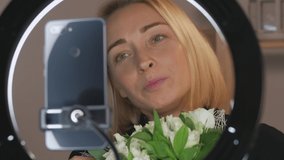 Female blogger with a bouquet of flowers live using a smartphone and led flashlight