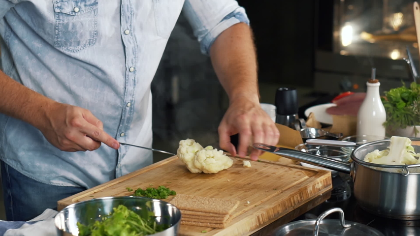 Cook in kitchen is cooking cauliflower, steam is on, man is cutting cauliflower into small pieces with sharp knife, healthy food, home cooking, diet, diet food, vegetarian food, vitamin-rich vegetable Royalty-Free Stock Footage #1044383530