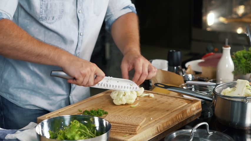 Cook in kitchen is cooking cauliflower, steam is on, man is cutting cauliflower into small pieces with sharp knife, healthy food, home cooking, diet, diet food, vegetarian food, vitamin-rich vegetable | Shutterstock HD Video #1044383530