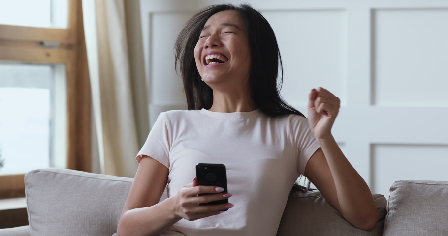 Excited young asian lady user winner hold smartphone feel amazed with good surprise social media news mobile online bid app win looking at cellphone laughing celebrating success victory concept Royalty-Free Stock Footage #1044388165