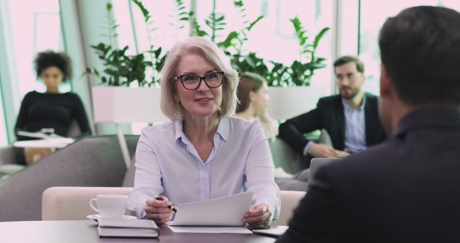 Smiling older mature business woman employer hr manager staffing holding cv checking male candidate resume asking questions during job interview office meeting, work placement and recruitment concept Royalty-Free Stock Footage #1044388261