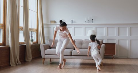 Happy funny barefoot family young asian mother nanny and cute small vietnamese kid girl child daughter playing running having fun in modern living room on warm floor enjoy leisure activity together