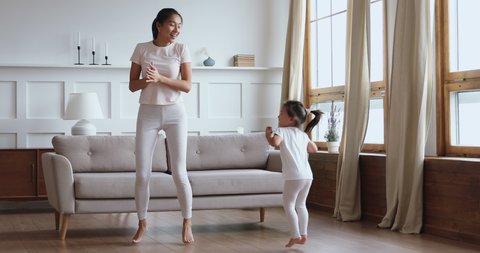 Carefree healthy fit young adult asian mom and child daughter having fun dancing together, happy vietnamese family mother play jump with cute little kid girl enjoy leisure lifestyle activity at home