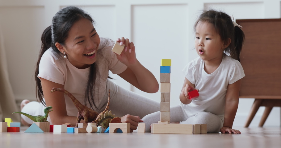 Happy vietnamese family asian mum daycare babysitter playing with focused cute small kid daughter help building castle of wooden blocks having fun talking laughing lying on warm floor in living room Royalty-Free Stock Footage #1044388333
