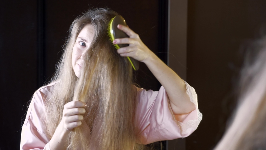 Unhappy Woman with Dry Brittle Hair Checking Her Tangled Hair in Mirror. Concept of Hair Care and Using Cosmetics for Strong Hair, Brittle Tips | Shutterstock HD Video #1044393067