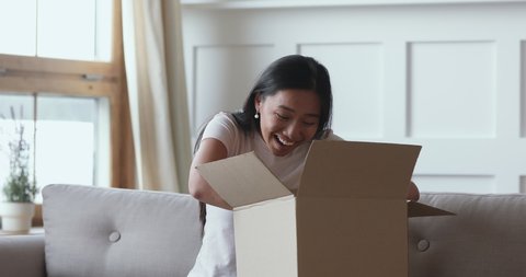 Excited asian female consumer opening parcel cardboard box receiving online shop fragile postal shipment order, happy ethnic girl customer satisfied with good purchase fast courier delivery concept