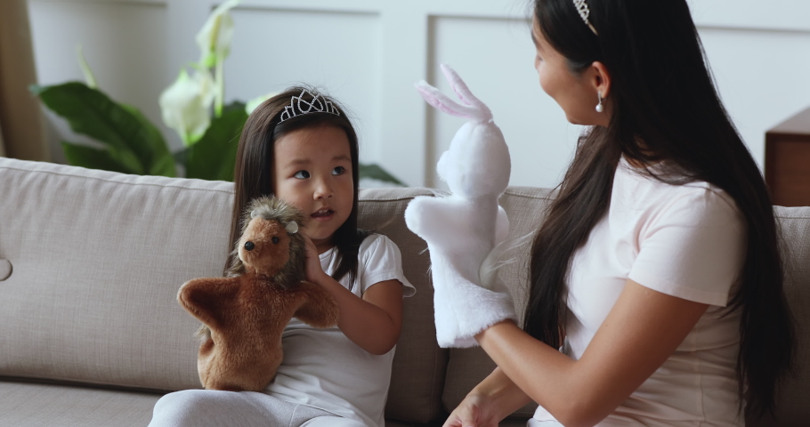 Happy asian young mom babysitter and cute small child daughter wear crowns play toys, funny little vietnamese kid girl hold puppet on hand having fun with mother enjoy lifestyle game together at home Royalty-Free Stock Footage #1044395578