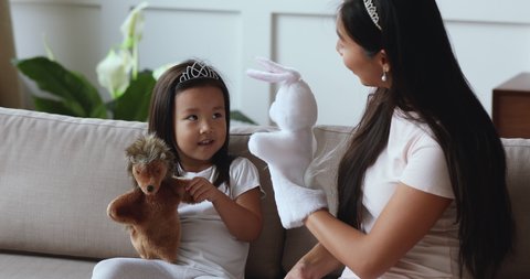 Happy asian young mom babysitter and cute small child daughter wear crowns play toys, funny little vietnamese kid girl hold puppet on hand having fun with mother enjoy lifestyle game together at home