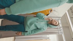 Portrait of young female in a hoodie looks at her reflection in the mirror of dressing room of a clothing boutique. Vertical screen orientation. 9:16. Slow motion. High resolution.