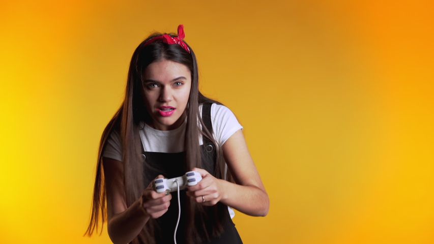 Pretty young girl playing video exciting game on Tv with joystick on yellow studio wall. Using modern technology.