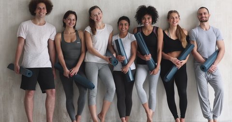 Multi-ethnic girls and guys leaned on wall smiling pose for camera, before or after work out people in sportswear holds yoga mats looking happy and healthy, well-being, hobby, sports lifestyle concept