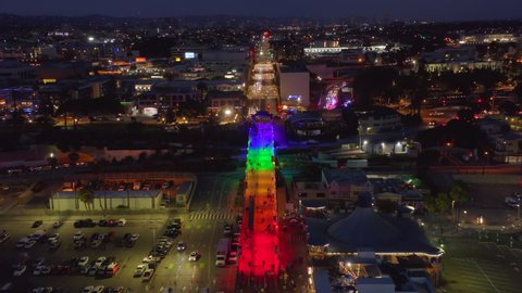LGBT pride flag or gay pride flag colors are highlighting the famous Santa Monica Pier in Los Angeles, California, USA. Aerial footage showing the night city top-down and the rainbow flag illumination Stockvideó