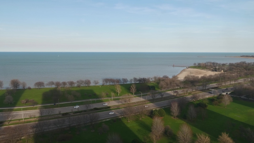 Chicago, IL - April 8th, 2017: Cars zoom by on Lake Shore Drive on a sunny spring day along the lakefront as the moon rises above the horizon and the sun casts long building shadows on the trees below