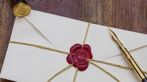 Love letter envelope sealed with thread and red wax heart shaped seal and quill pen. Zoom out shot