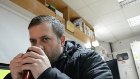 tired security guard drinks a hot drink from red сup. steam rises over a cup.