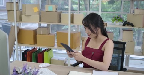 Slow motion female business women as a  small SME with online sales she was busy with the ordered and phone called and packing. On top of table are a lots of boxes ready to ship.