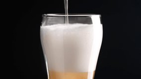Cold light craft beer is poured into a glass. Beer fluffy foam rises to the edge of the glass. Horizontally oriented video on a black background. 4K UHD video 3840x2160