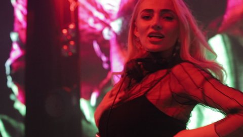 Attractive Dancing Blonde In The Club, Neon Light, Motion Effects. DJ Girl Dancing With Headphones On Neck.