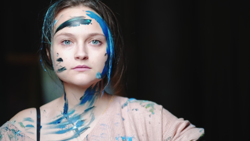 Art power. Stress relief. Confident woman making lines on face with blue paint.
