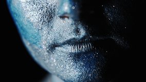 Fantasy makeup. Skincare procedure. Woman with face in blue shimmering paint on dark background.