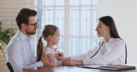 Happy cute little child girl patient and female pediatrician give high five after pediatric checkup, woman doctor wear white coat listening heartbeat with stethoscope on consultation kid with parent