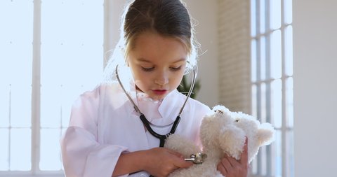 Cute adorable little preschool kid girl wear white medical uniform holding stethoscope listening sick toy teddy bear patient, smart small child playing hospital game as doctor pretend nurse concept