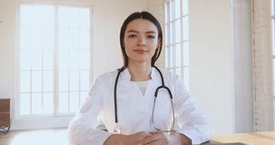 Young female doctor wear white medical uniform looking at camera talking to webcam helping patient during distance video conference call chat provide medical services teach online by webinar concept