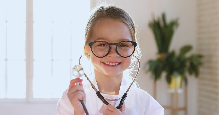 Funny little child girl wear medical uniform glasses holding stethoscope playing game as doctor, happy cute adorable small preschool kid pretending medic nurse looking at camera, close up portrait Royalty-Free Stock Footage #1044437113