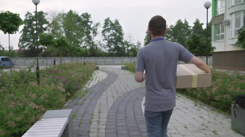Young bearded courier carrying paper boxes and looking for house of recipient. Handsome man in casual outfit delivering parcels and holding clipboard with all information.