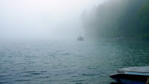 Fisherman in boat is fishing on a beautiful foggy Minnesota lake in early morning. Zoom in.