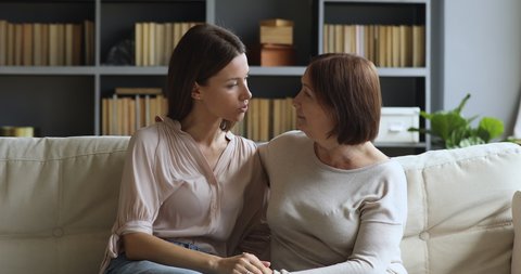Loving beautiful older mature mother and young adult daughter talking bonding sit on sofa at home, understanding two generation women family having trust honest conversation give support concept