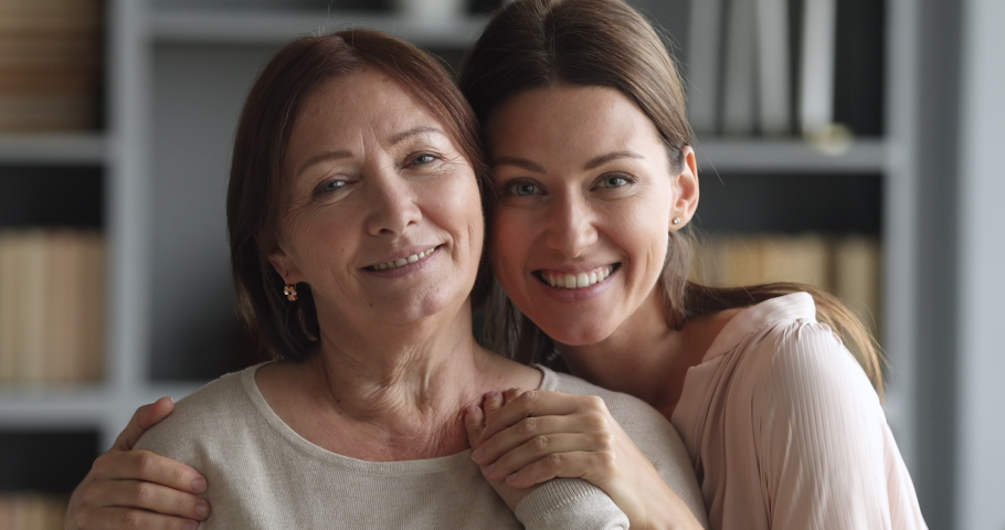 Beautiful caring adult daughter hugging senior mature mum bonding together looking at camera indoors, loving smiling two older and young age generation women embracing at home, close up portrait Royalty-Free Stock Footage #1044454945