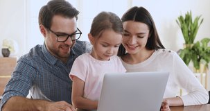 Happy family of three young adult parents and cute kid daughter bonding talking using laptop computer at home, smiling mom dad with preschooler child browse internet watch video on technology device