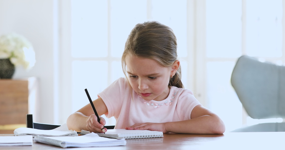 Cute smart primary school child girl learning writing doing math homework sit at home table, adorable pretty little preschool kid studying alone making notes, children elementary education concept Royalty-Free Stock Footage #1044455035
