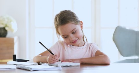 Cute smart primary school child girl learning writing doing math homework sit at home table, adorable pretty little preschool kid studying alone making notes, children elementary education concept