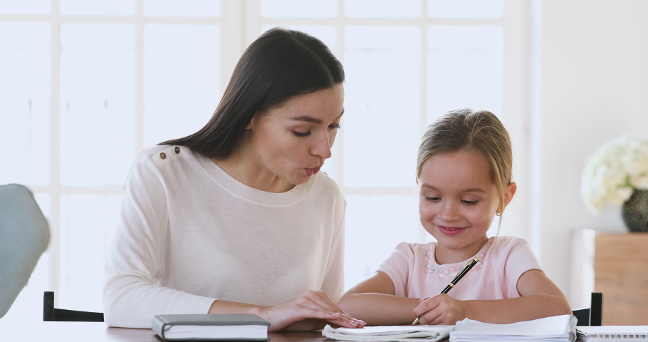 Happy adult mother teacher babysitter and cute preschool or school child girl daughter studying together learning writing giving high five celebrate homework well done good education results concept Royalty-Free Stock Footage #1044455038
