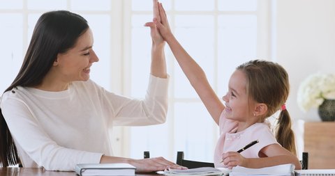 Happy adult mother teacher babysitter and cute preschool or school child girl daughter studying together learning writing giving high five celebrate homework well done good education results concept