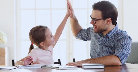 Adult dad or teacher and happy cute preschool school child girl daughter study together learn write give high five celebrate successful class finish homework, parent help child with education concept