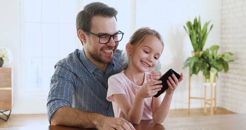 Young parent dad and cute small kid daughter bloggers recording lifestyle vlog on smartphone talking looking at phone using funny application having fun with tech education concept sit at home table