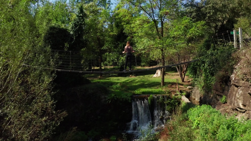 Aerial flight under the bridge view of girl standing on suspension bridge drone.