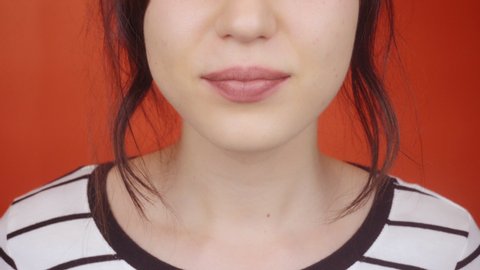 Young brunette girl with gorgeous lips on a bright red background. Happy woman sends an air kiss to the camera, lips closeup.