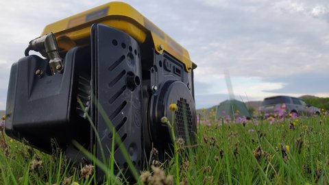 Close up of gas diesel mobile portable electricity generator work on grass. Gasoline fuel powered portable generator give electric energy current for camping. Background: grass, tent, car. Outdoor.
