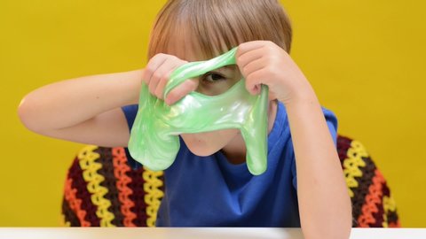Funny blonde boy playing with slime. Anti stress toys for kids. Cute kid enjoying slime toy. Boy sits at table at home