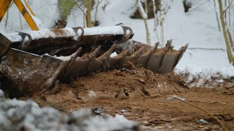 A bulldozer removes a layer of soil in a snowy forest. Construction of the road among the wild. Bucket close-up
