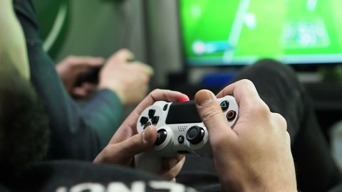 Close view of a gamer's hands playing soccer (football) simulator video game on console using joystick. russia, saratov - november, 2018